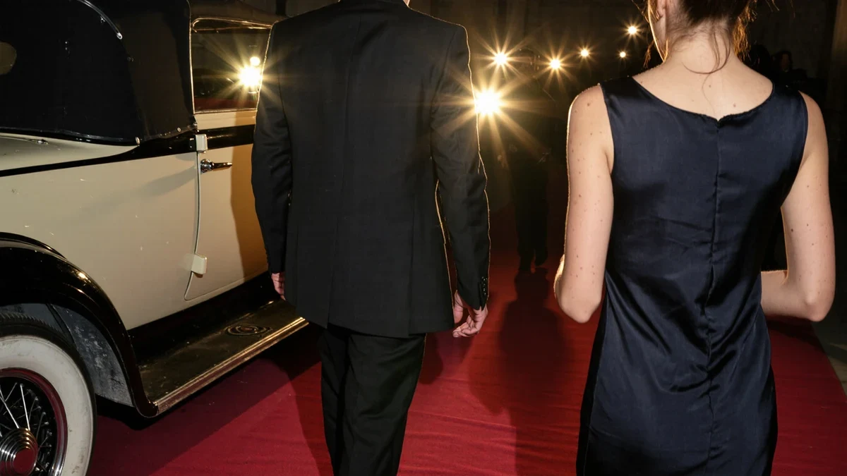 Golden flash bulbs pop along a velvet-roped arrivals line as an elegant couple steps from a vintage convertible, marquee glow warming the night.