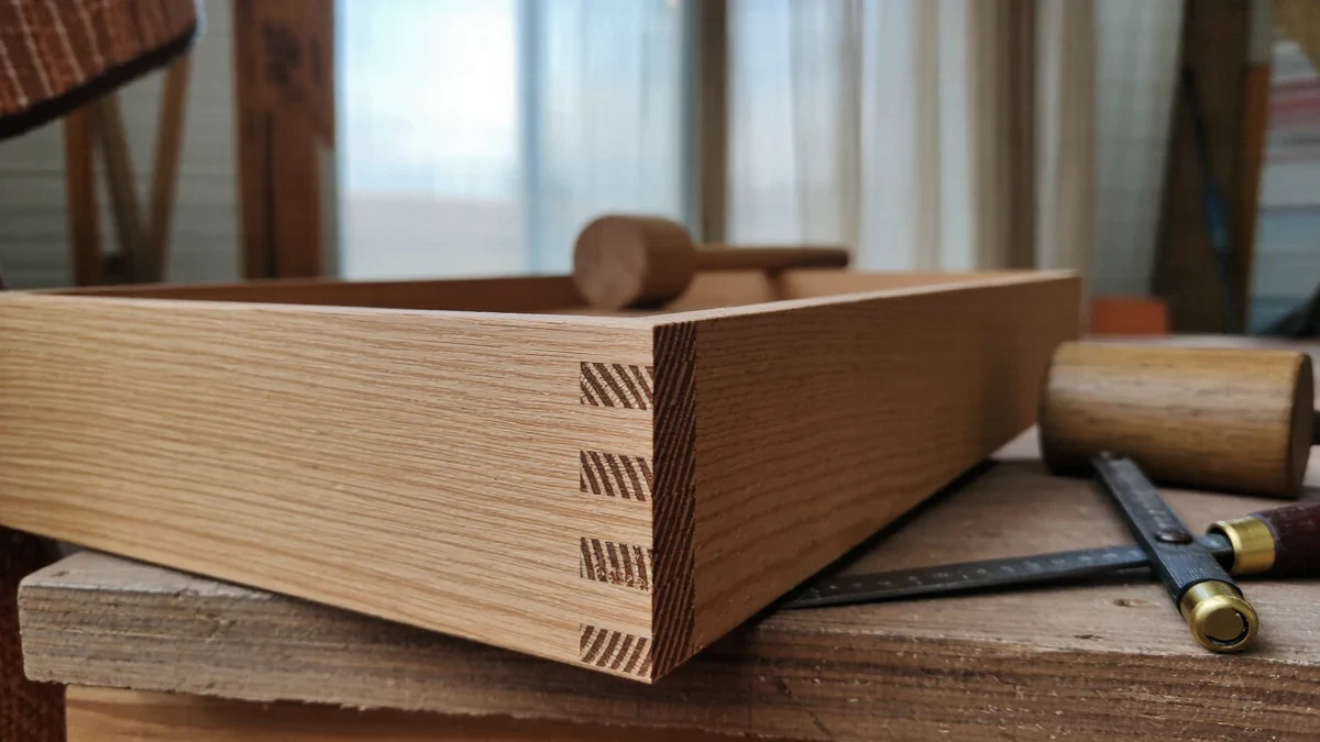 A maker's studio bathed in raking light, curls of wood on the bench, a drawer's dovetails mid-assembly, a craftswoman fitting a tenon into its mortise by hand.