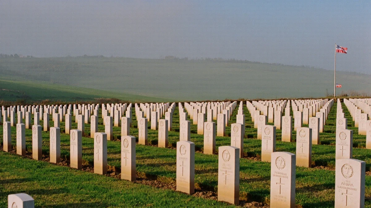 A national cemetery avenue in early light, rows of plain white markers receding behind flags at half-staff, a visitor standing quietly among them.